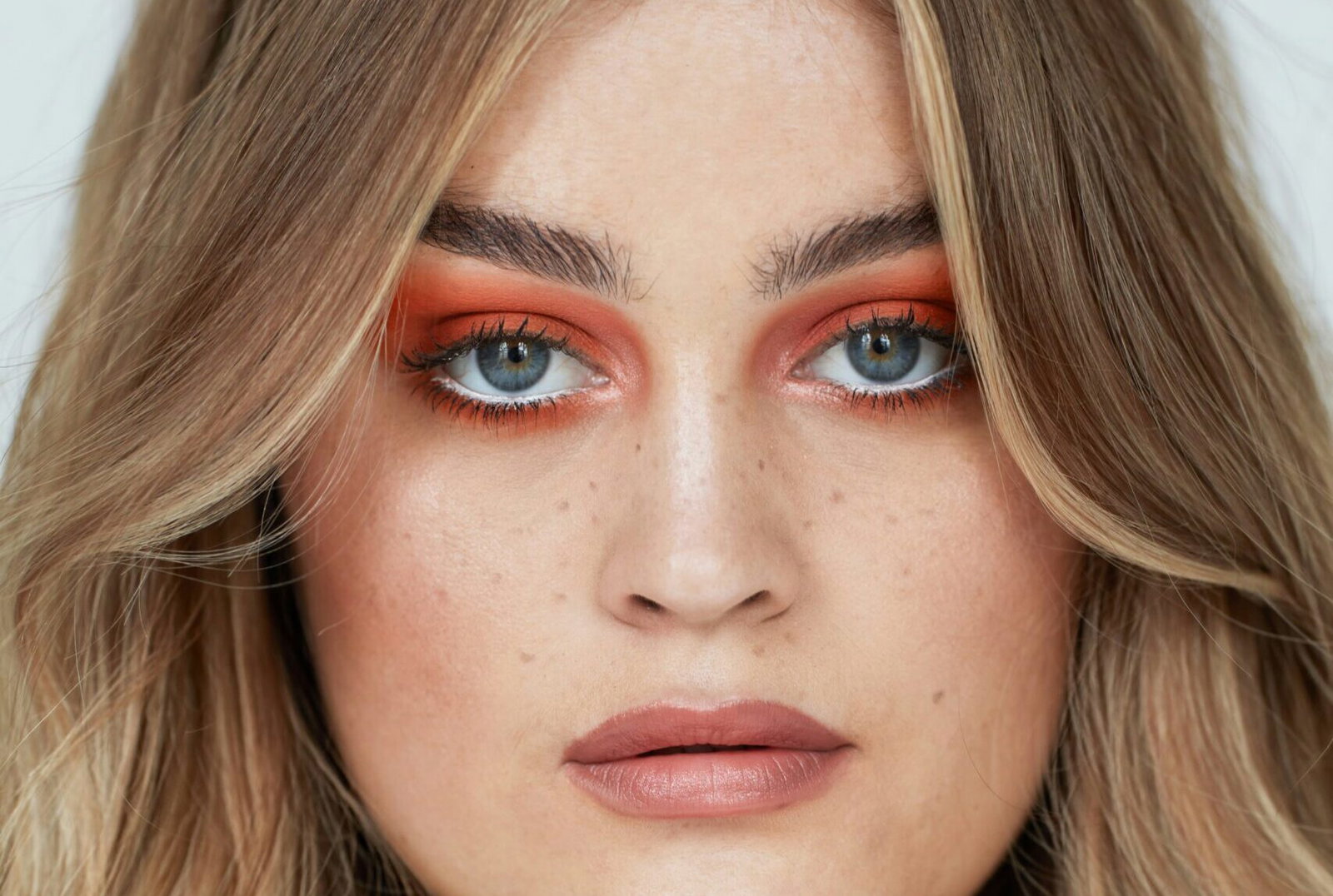 Woman wearing bold orange-red eyeshadow with glossy, softly waved hair.