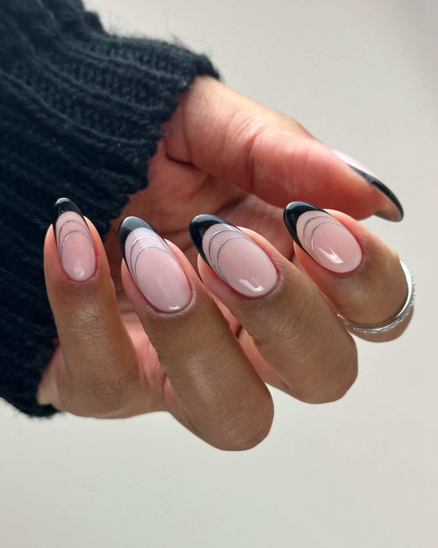 Almond nails with glossy black French tips and fine silver curved line details.