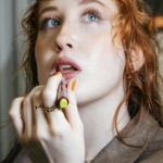 Red-haired model applying lip colour.
