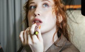 Red-haired model applying lip colour.