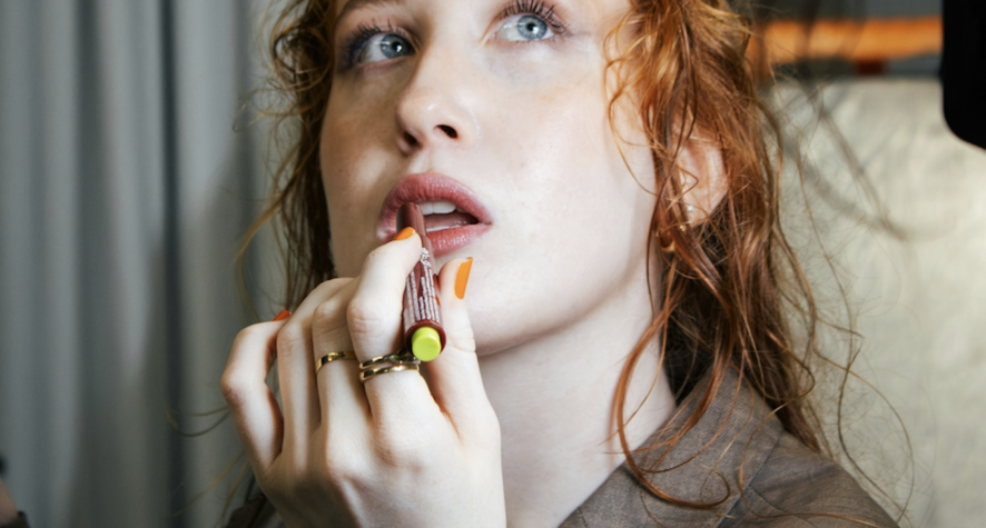 Red-haired model applying lip colour.