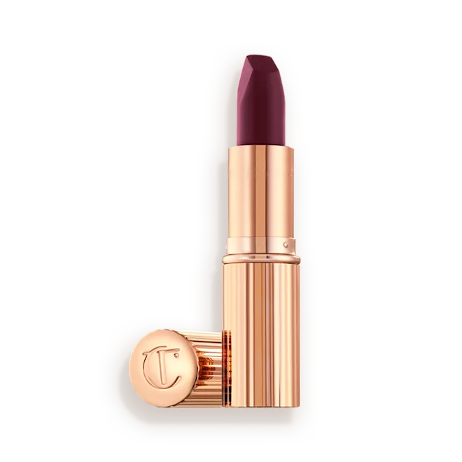Charlotte Tilbury Matte Revolution lipstick in Festival Magic, showing the deep berry bullet with its rose gold cap alongside.