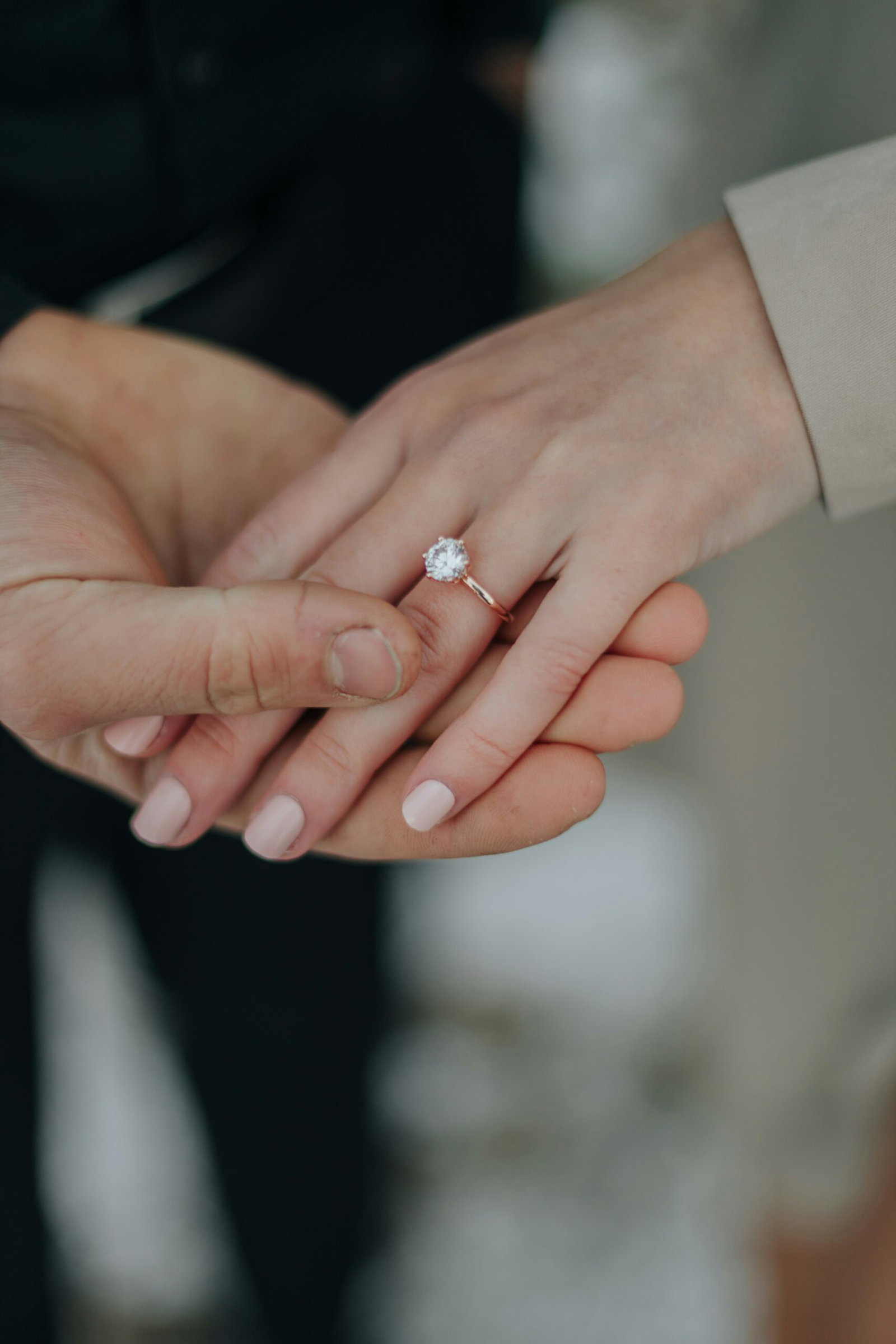 Couple holding hands outdoors, showing a diamond engagement ring and a natural nude manicure.
