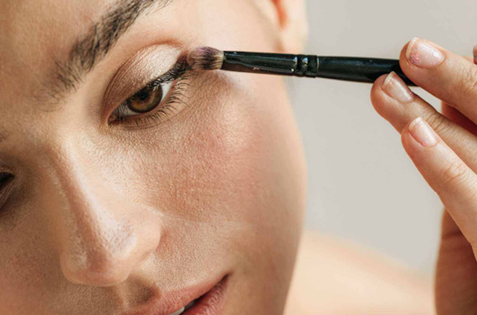 Close-up of a woman applying soft brown eyeshadow with a makeup brush for a glamorous evening look.