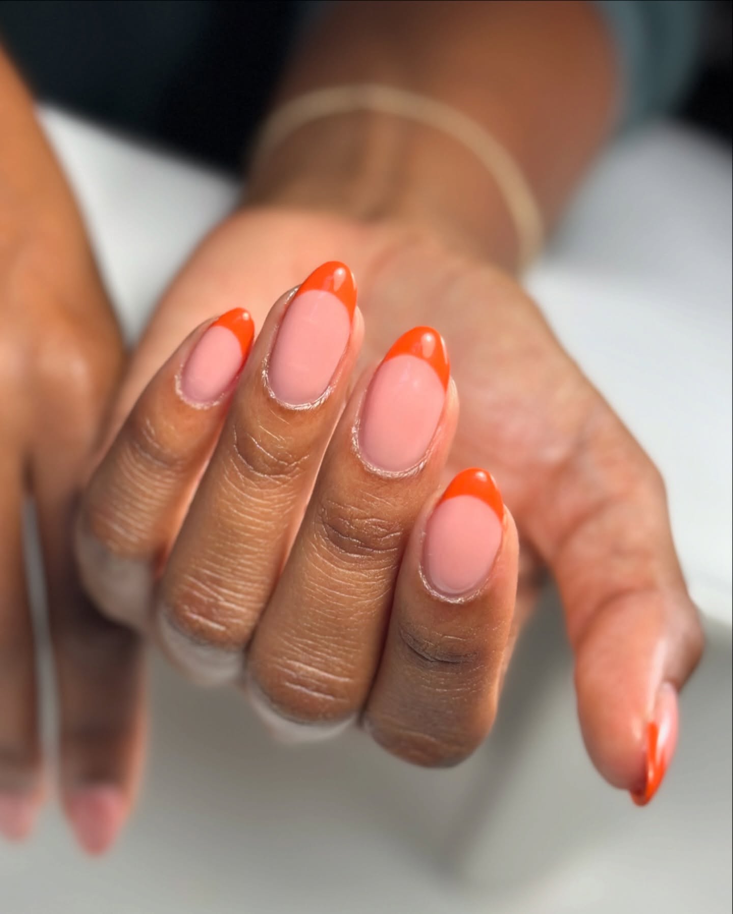 Almond-shaped nails with glossy pumpkin orange French tips over a soft pink base