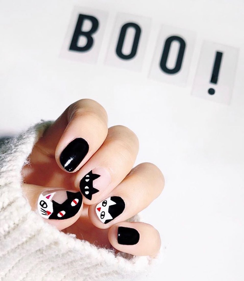 Short black Halloween nails featuring playful black and white cat faces on a nude base