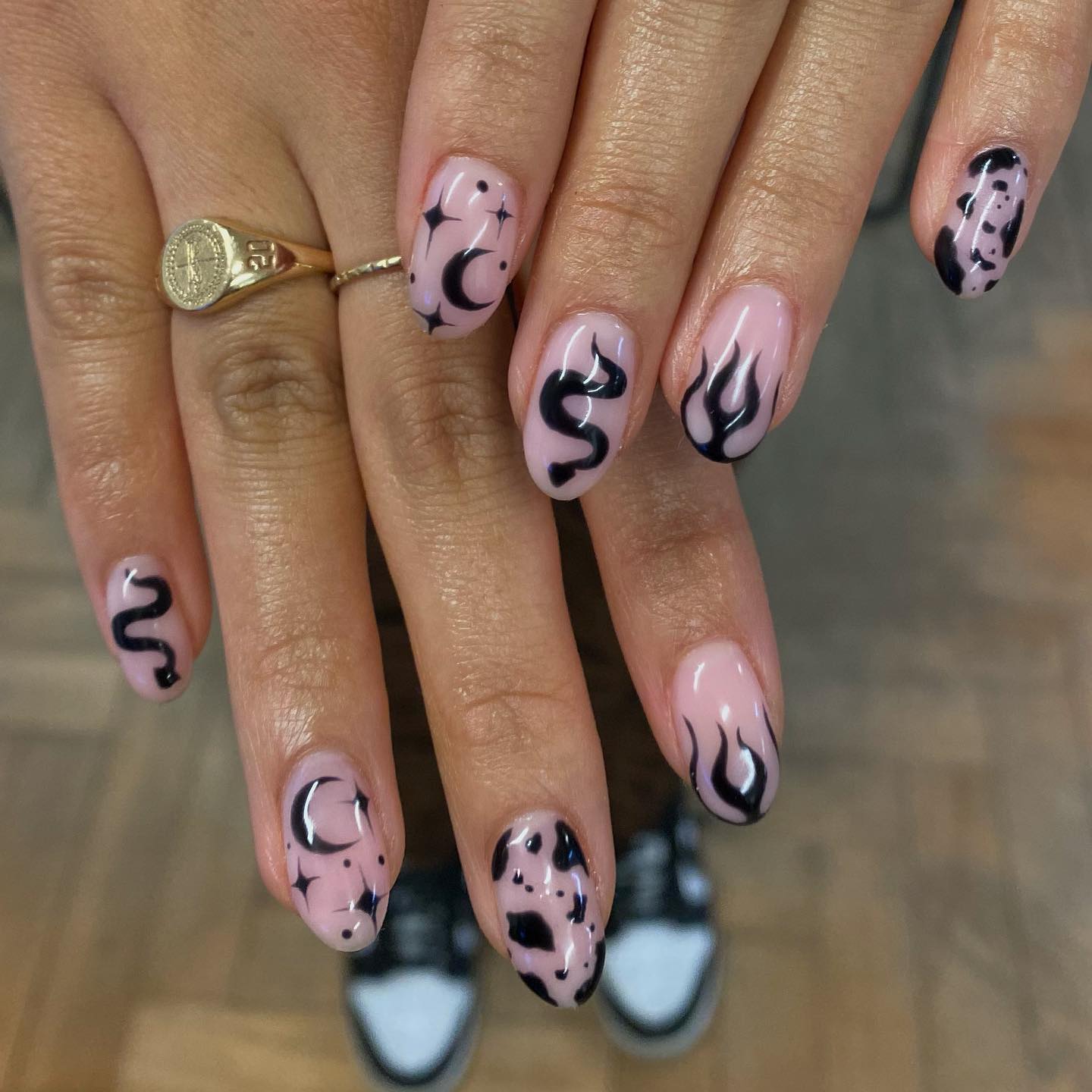 Nude pink Halloween nails decorated with black snakes, flames, crescent moons and stars