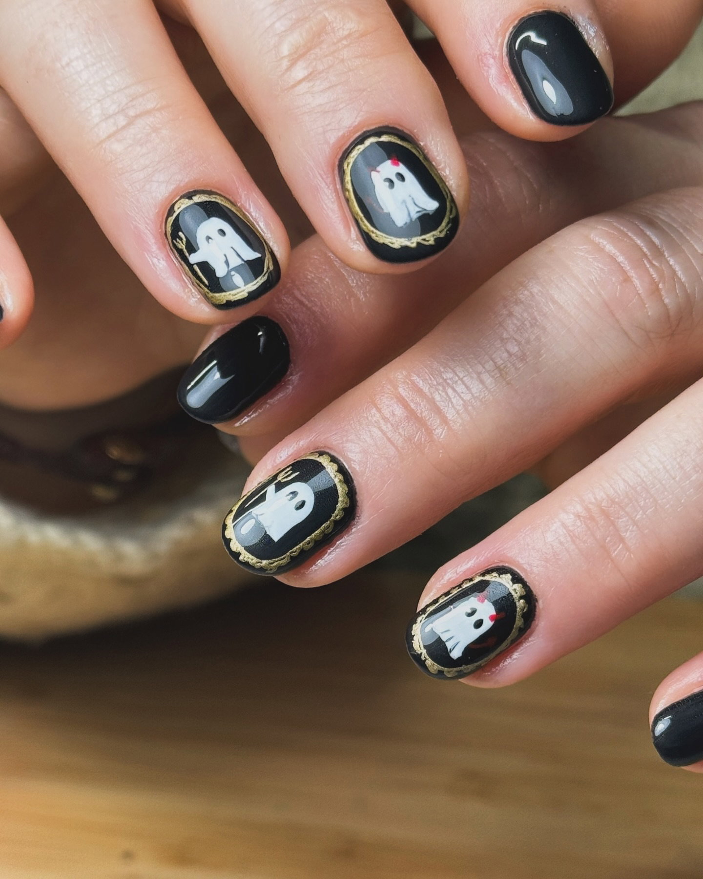 Glossy black Halloween nails with white ghosts inside delicate gold frames