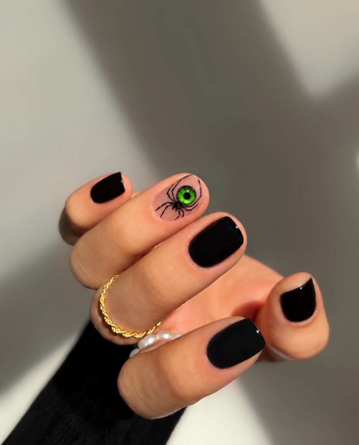 Short glossy black Halloween nails with a green-eyed spider accent on a nude nail