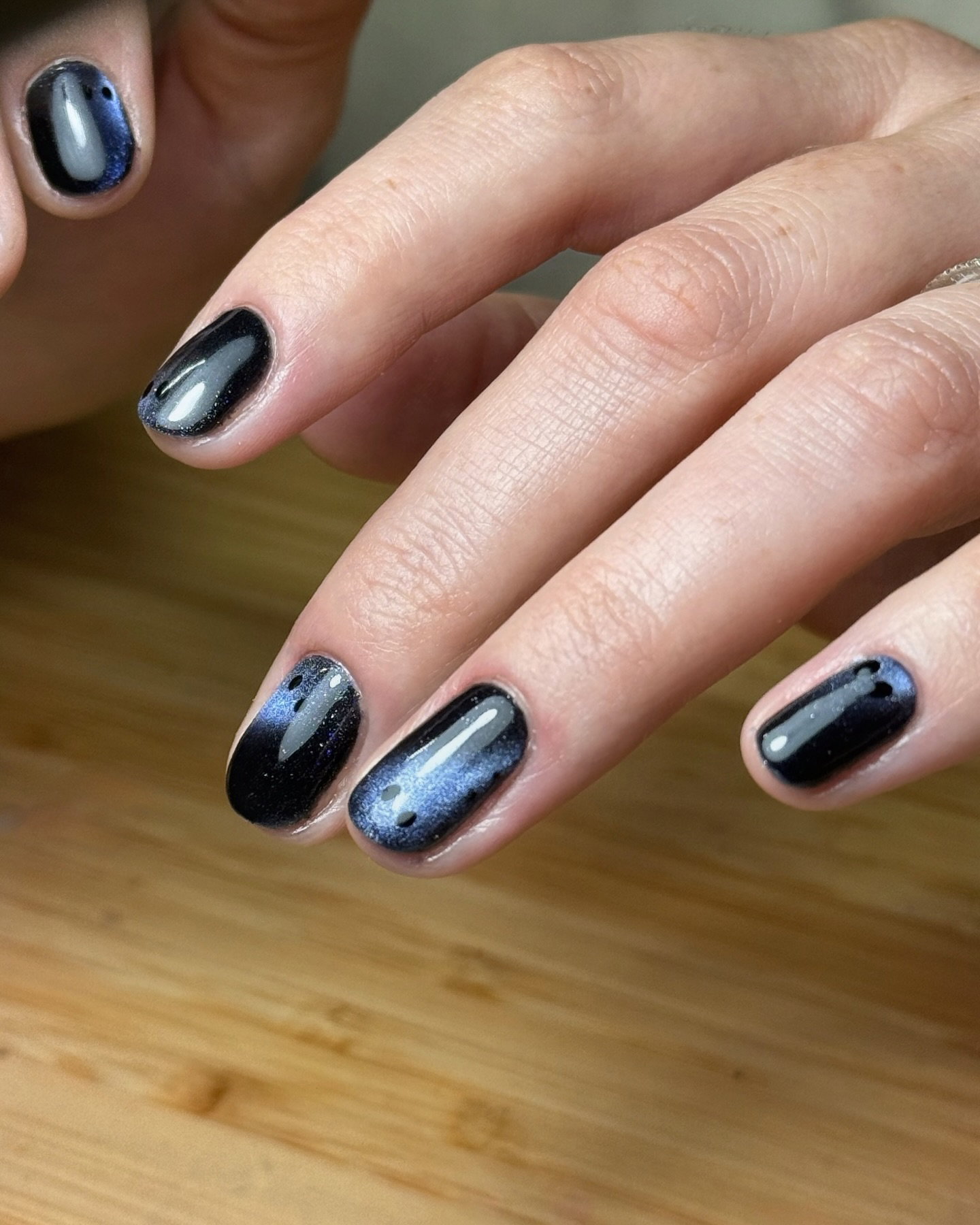 Short black cat-eye nails with smoky blue-grey shimmer and subtle ghostly faces