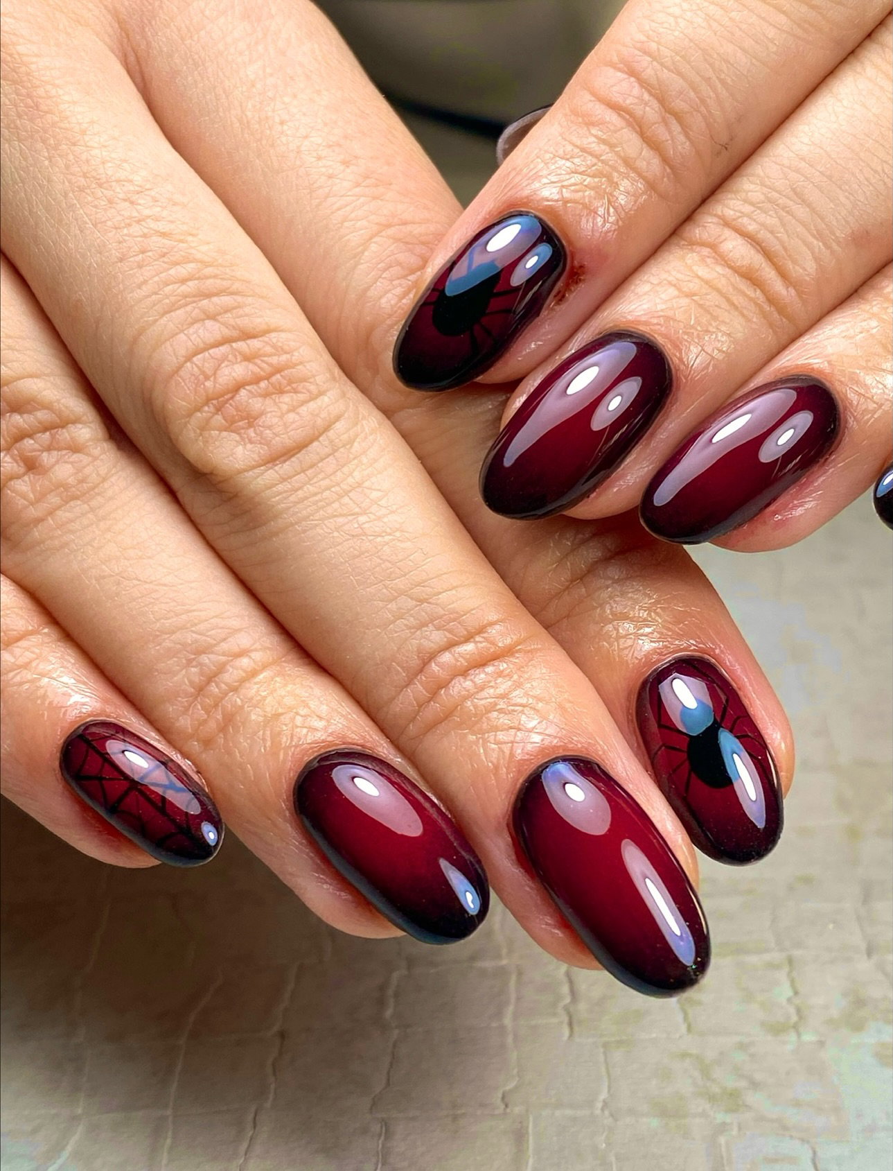 Glossy burgundy almond nails with black spider and cobweb designs