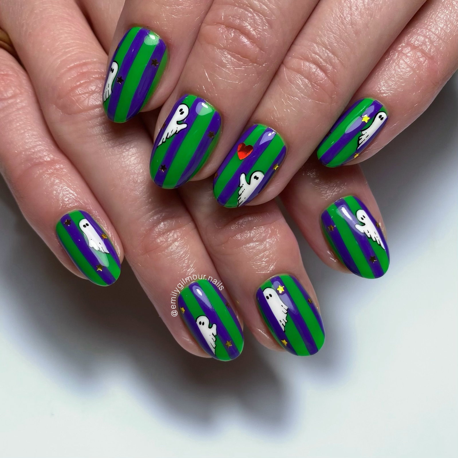 Bright green and purple striped Halloween nails with white peekaboo ghosts and tiny stars