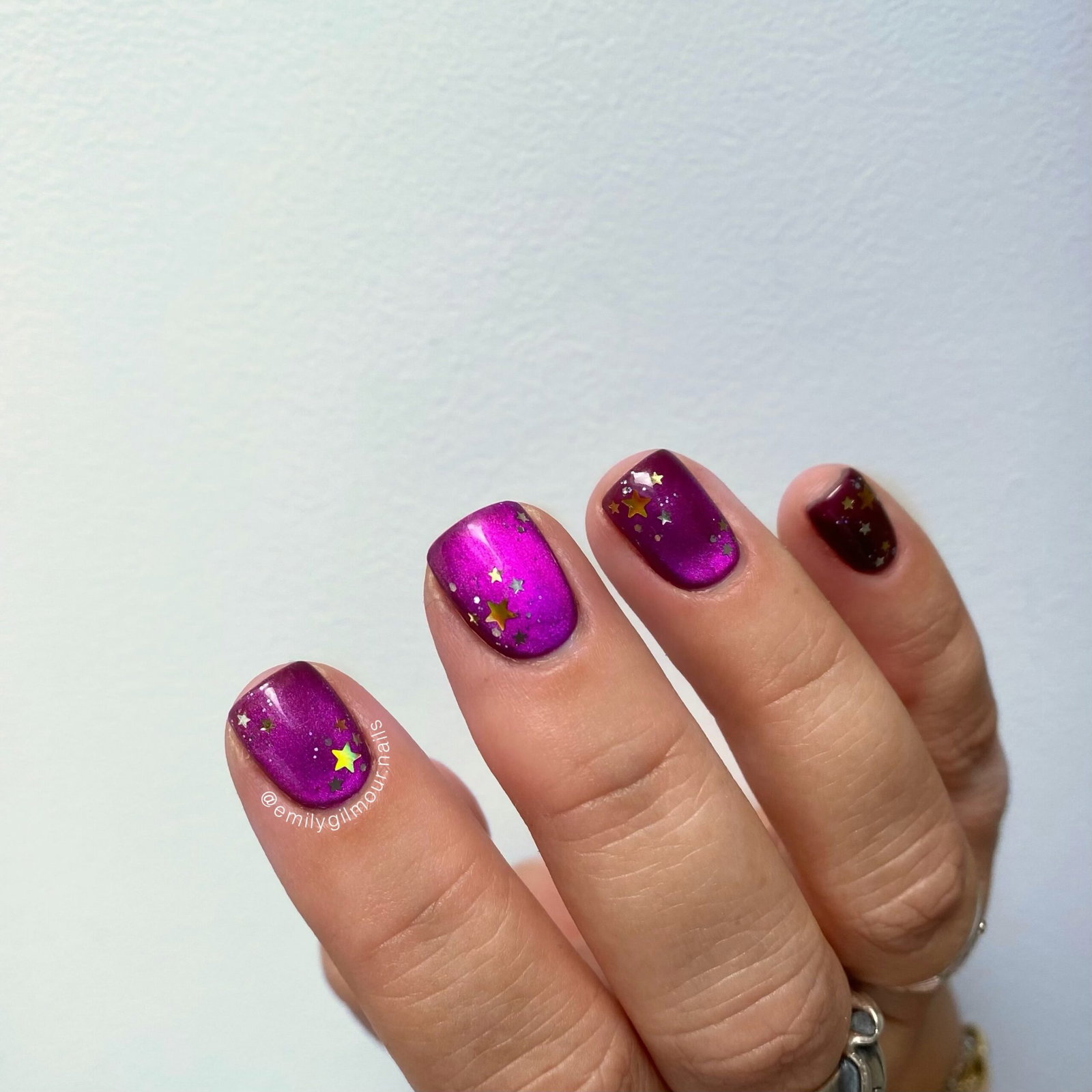 Short metallic purple cat-eye nails decorated with scattered gold stars