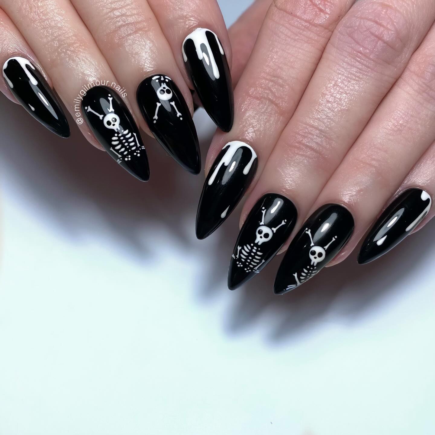 Long glossy black stiletto nails featuring white skeletons and dripping nail art