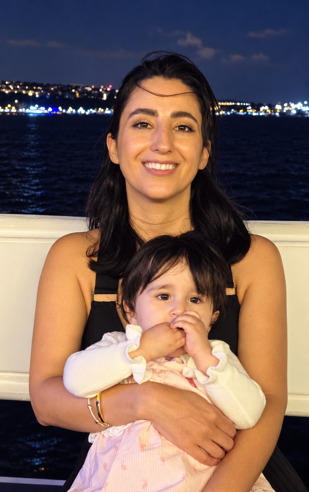 Cool Mood founder Mina Akbari smiling while holding her young daughter on a boat, with the water and evening city lights behind them.