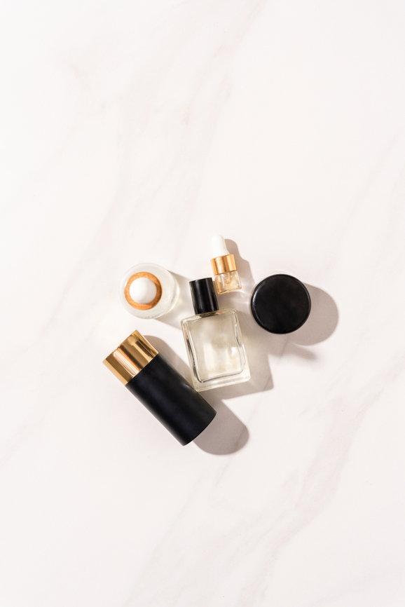 Flat lay of skincare and beauty products in black, glass and gold packaging on a pale marble background.