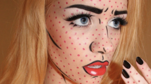 Close-up of a woman wearing pop art Halloween makeup with red polka dots, bold black comic-book outlines, dramatic lashes and bright red lipstick.