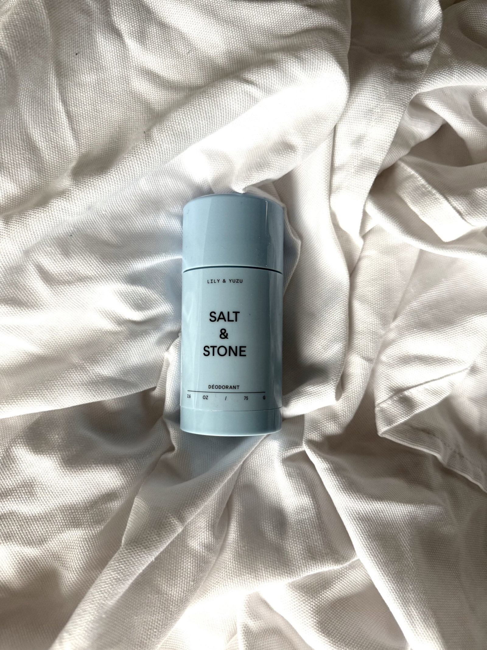 Salt & Stone Lily & Yuzu natural deodorant in its pale blue packaging, photographed on softly draped white fabric.