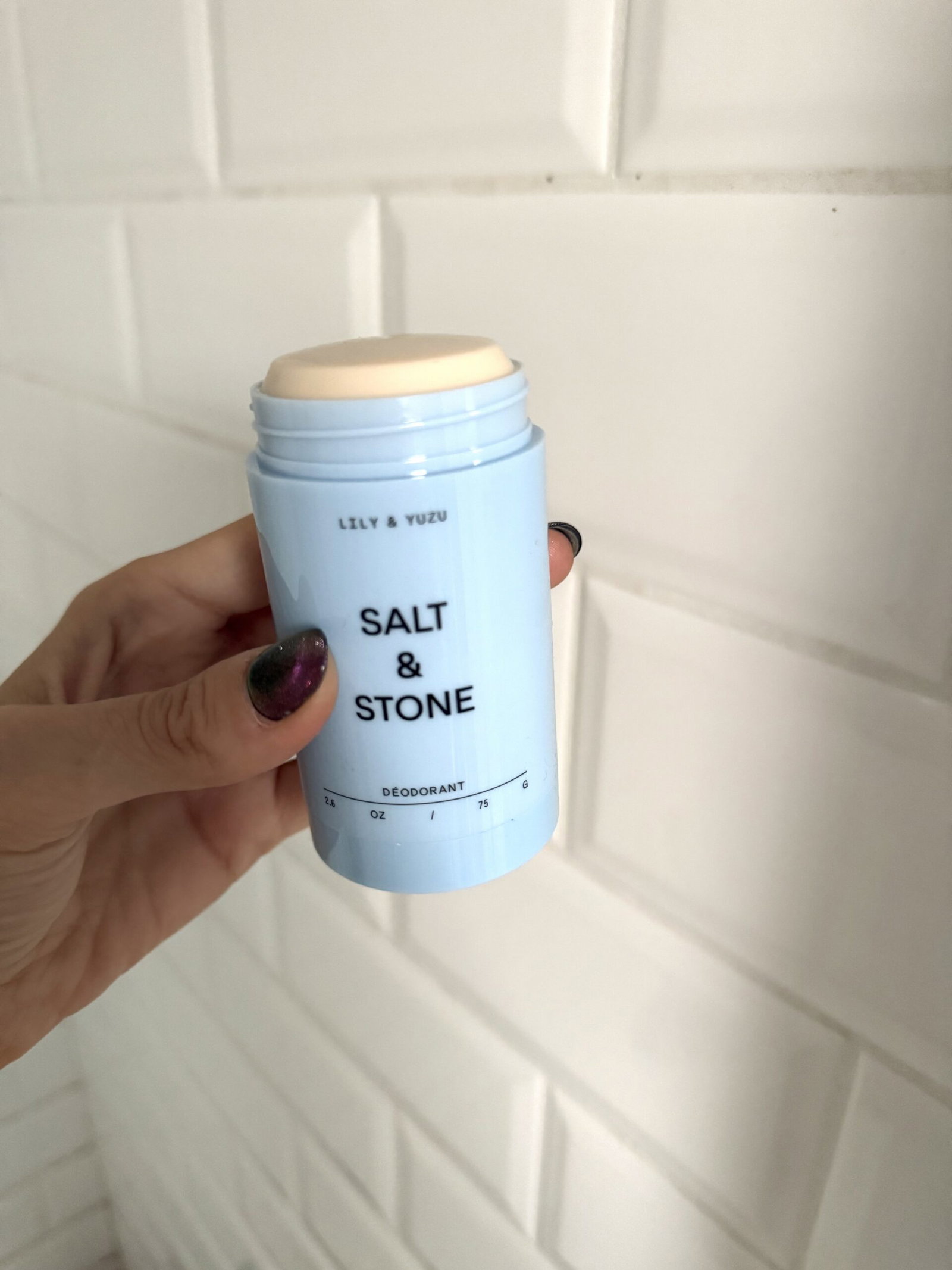 Open Salt & Stone Lily & Yuzu deodorant stick held in a hand, showing its creamy formula and pale blue packaging.