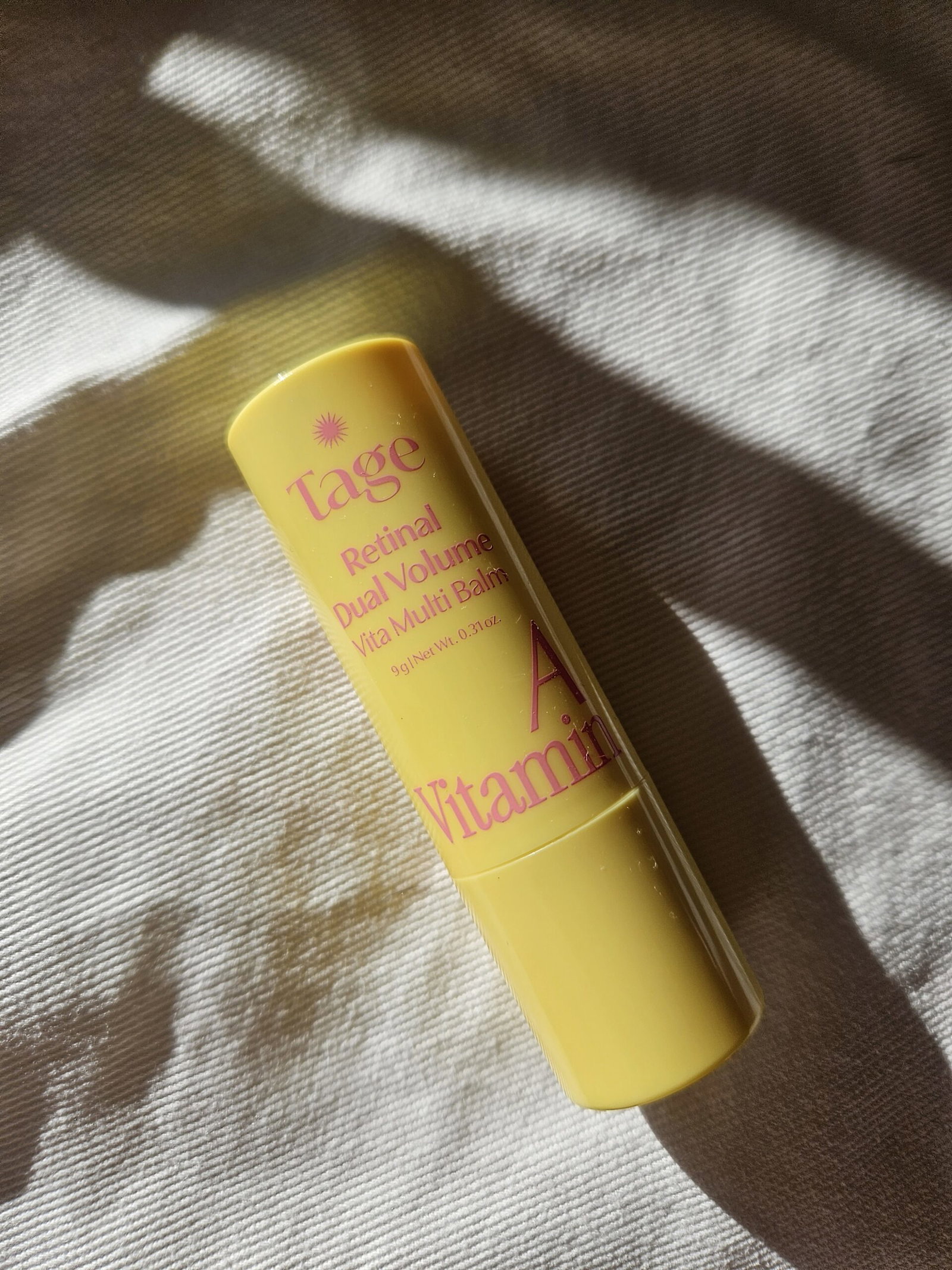 Tage Vita A Retinal Dual Volume Multi Balm Stick in yellow packaging with pink lettering, photographed in natural sunlight.