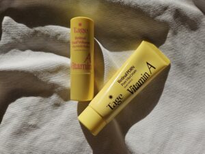 Tage Vita A Retinal Multi Balm Stick and Retinal PDRN Pore Booster Cream in bright yellow packaging, photographed together in natural sunlight.