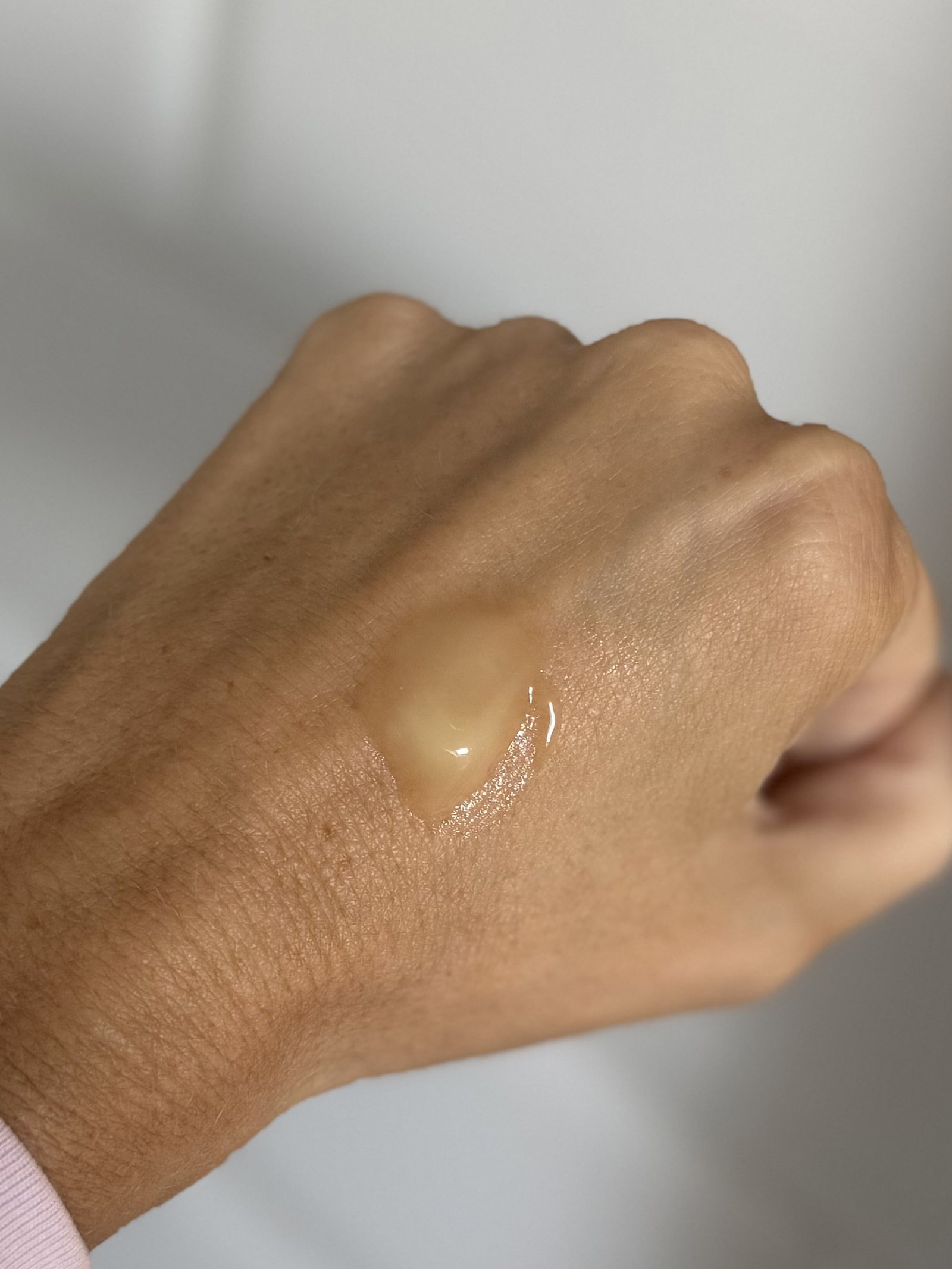 A small amount of The INKEY List Oat Balm Cleanser on the back of a hand, showing its pale golden, slightly runny balm consistency.